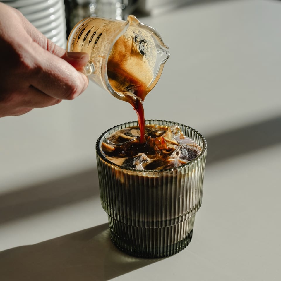 A hand pours espresso from a measuring cup into a glass of iced coffee at Fearless Coffee & Kitchen.