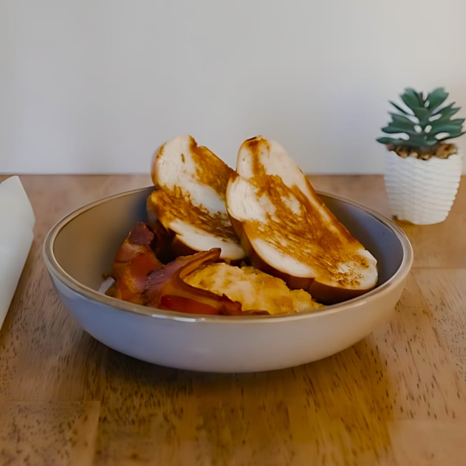 A bowl of scrambled eggs, bacon, and two slices of toasted bread on a wooden table.